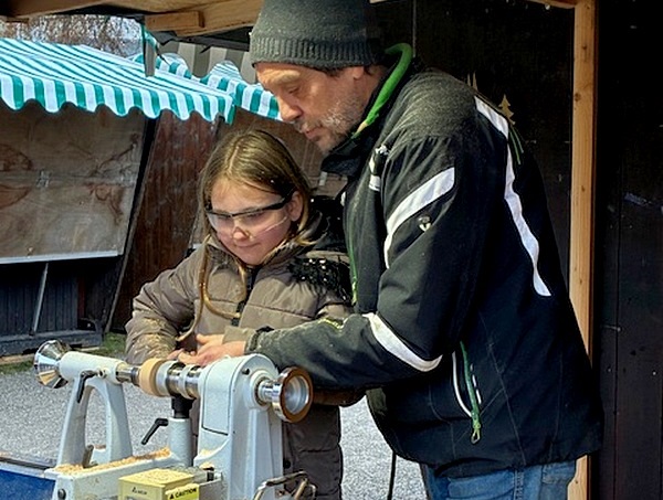 Ein Mädchen drechselt an einer Maschine unter Anleitung eines Mannes